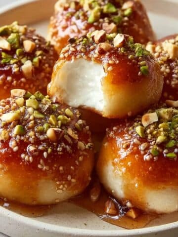 Ricotta pistachio honey bites drizzled with golden honey and topped with chopped pistachios, showing a soft creamy ricotta-filled center on a white plate in a close-up dessert shot.