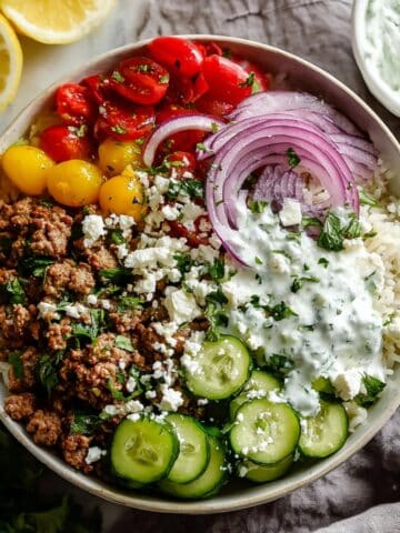 Ground turkey rice bowl with sliced cucumbers, cherry tomatoes, red onion, feta cheese, and creamy tzatziki sauce, served fresh and healthy