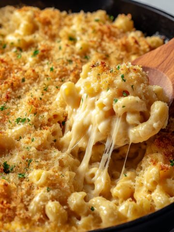 Creamy one-pan butter Parmesan pasta in black skillet with wooden spoon scooping macaroni showing melted cheese strings, topped with golden buttery breadcrumbs and fresh chopped parsley