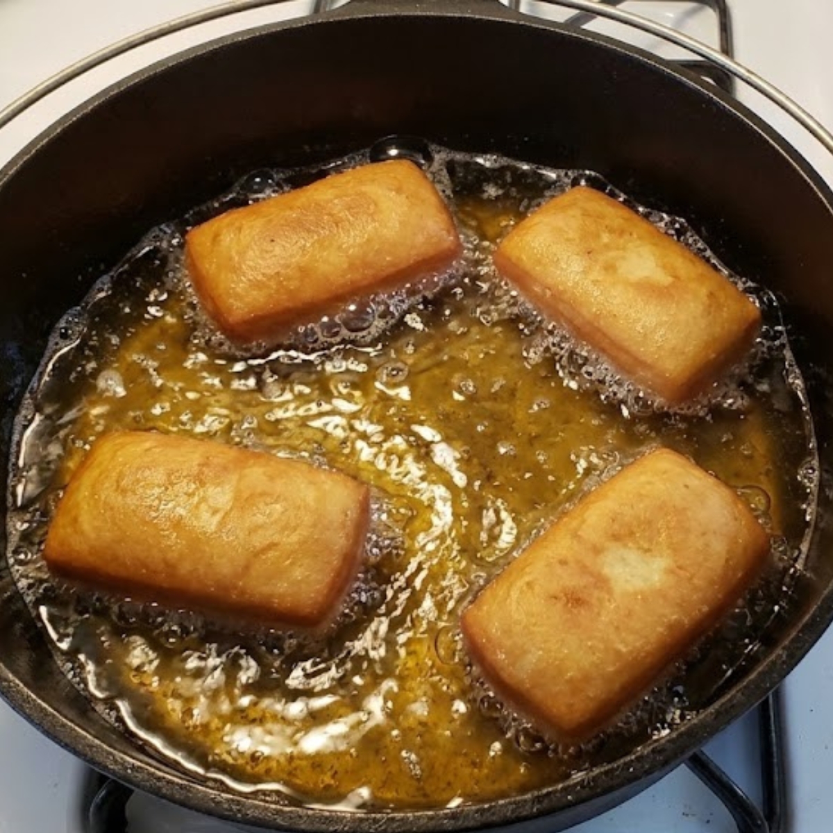 A close-up photo of donut bars frying in a pot of hot oil, turning golden brown.