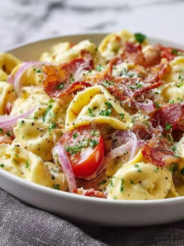 Grinder Tortellini Salad in a white bowl with cheese tortellini, crispy bacon, cherry tomatoes, red onion, parmesan, and fresh parsley in creamy dressing