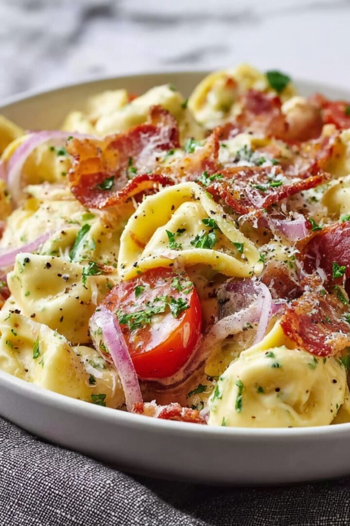 Grinder Tortellini Salad in a white bowl with cheese tortellini, crispy bacon, cherry tomatoes, red onion, parmesan, and fresh parsley in creamy dressing