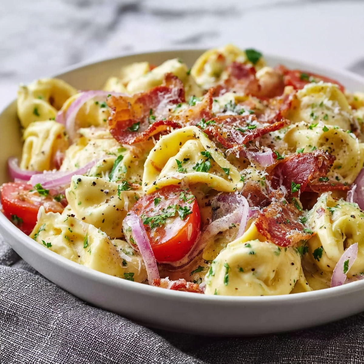 Grinder Tortellini Salad in a white bowl with cheese tortellini, crispy bacon, cherry tomatoes, red onion, parmesan, and fresh parsley in creamy dressing