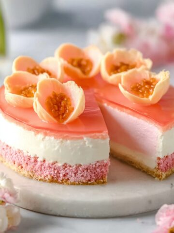 Hawaiian Guava Cake on a marble stand with pink chiffon layers, whipped cream filling, glossy guava gel topping, and fresh guava flower garnishes.