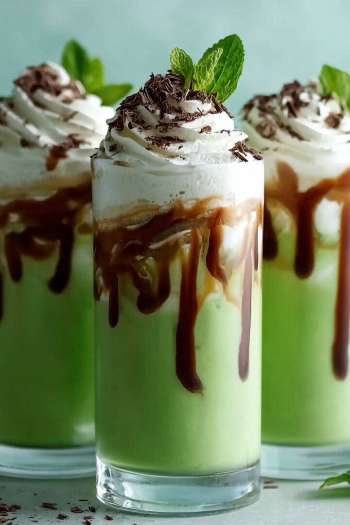 Irish Cream Soda in tall glasses with a vibrant green cream base, drizzled chocolate sauce, whipped cream, chocolate shavings, and fresh mint leaves.