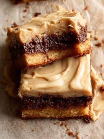 Two stacked salted caramel brown sugar pop tart cookie bars with a golden cookie base, dark brown sugar filling, and swirled caramel frosting on top, served on parchment paper on a wooden surface.