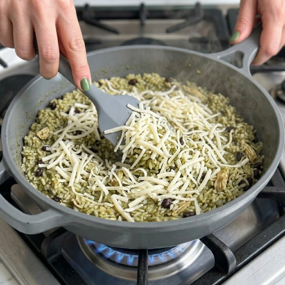 Tight zoom of hands with green nails scattering shredded white cheese over a hot chicken and rice skillet.