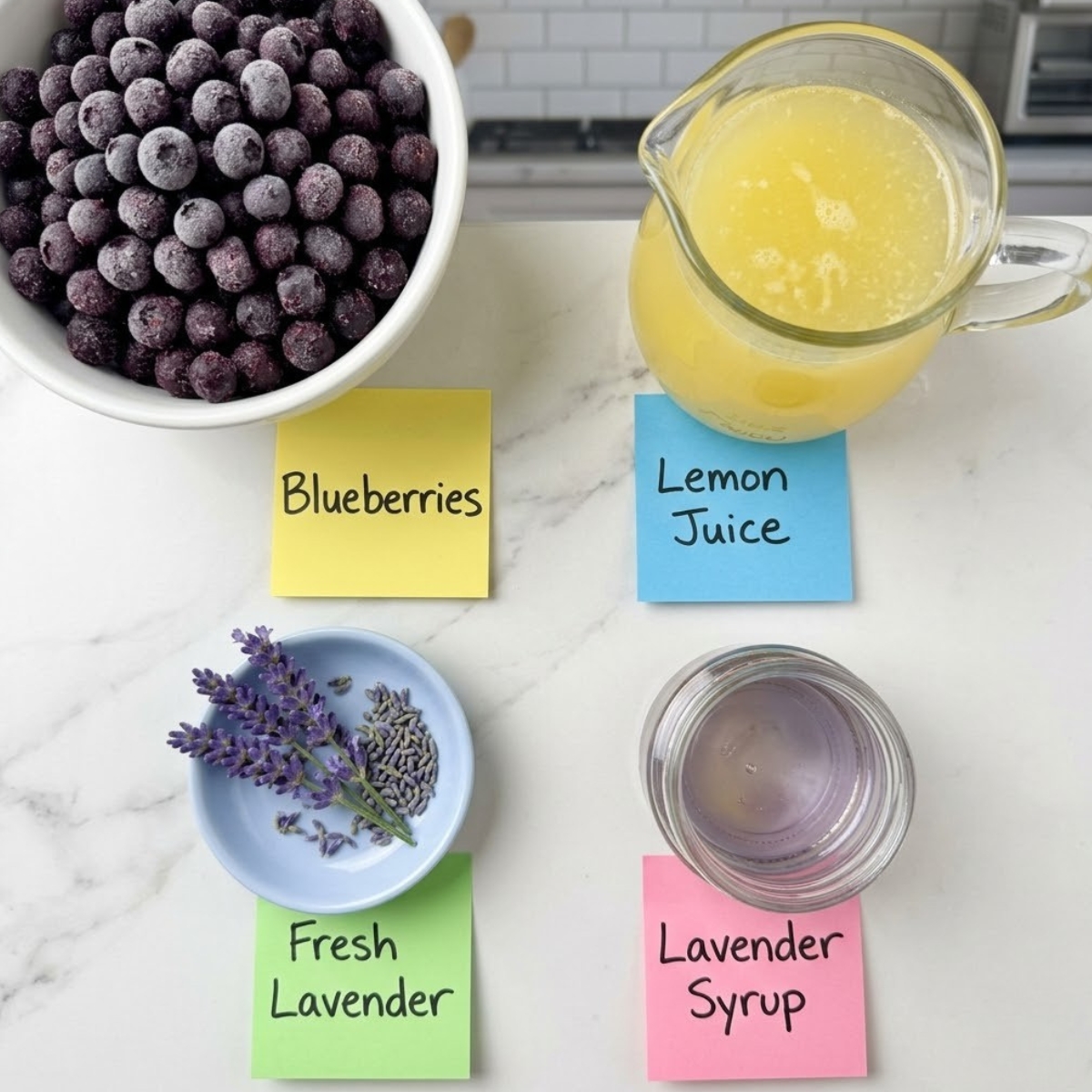 Flat lay of frozen blueberries, fresh lemon juice, lavender syrup, and lavender sprigs with handwritten labels on a marble counter.