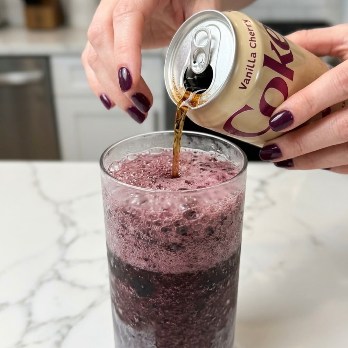 Tight zoom of hands with plum nails pouring fizzy soda into a purple cherry slushie base.