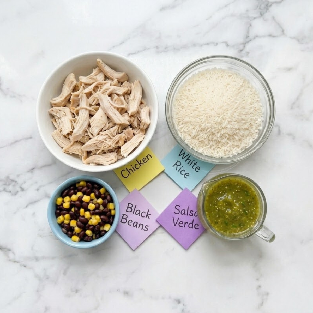 Flat lay of shredded chicken, uncooked rice, green salsa verde, and black beans with handwritten labels on a marble counter.