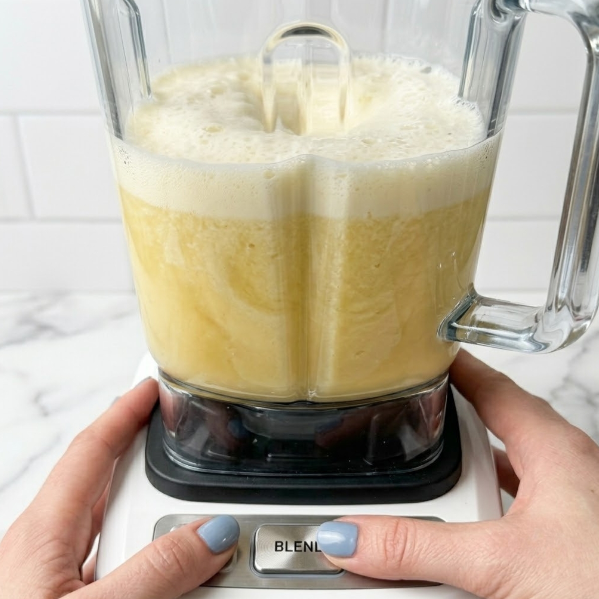 Tight close-up zoom of a blender processing pineapple juice and coconut milk into a frothy pale yellow beverage.