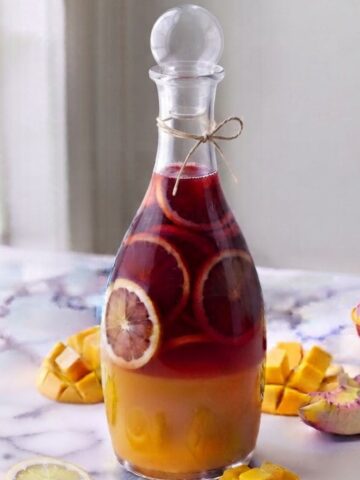 Peach Pomegranate Lemonade contained in a glass bottle on white marble kitchen counter with sliced peaches and