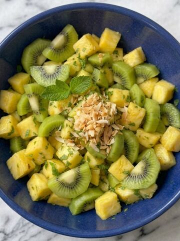 A close-up of Pineapple Kiwi Salad in a blue ceramic bowl placed on white marble kitchen counter.