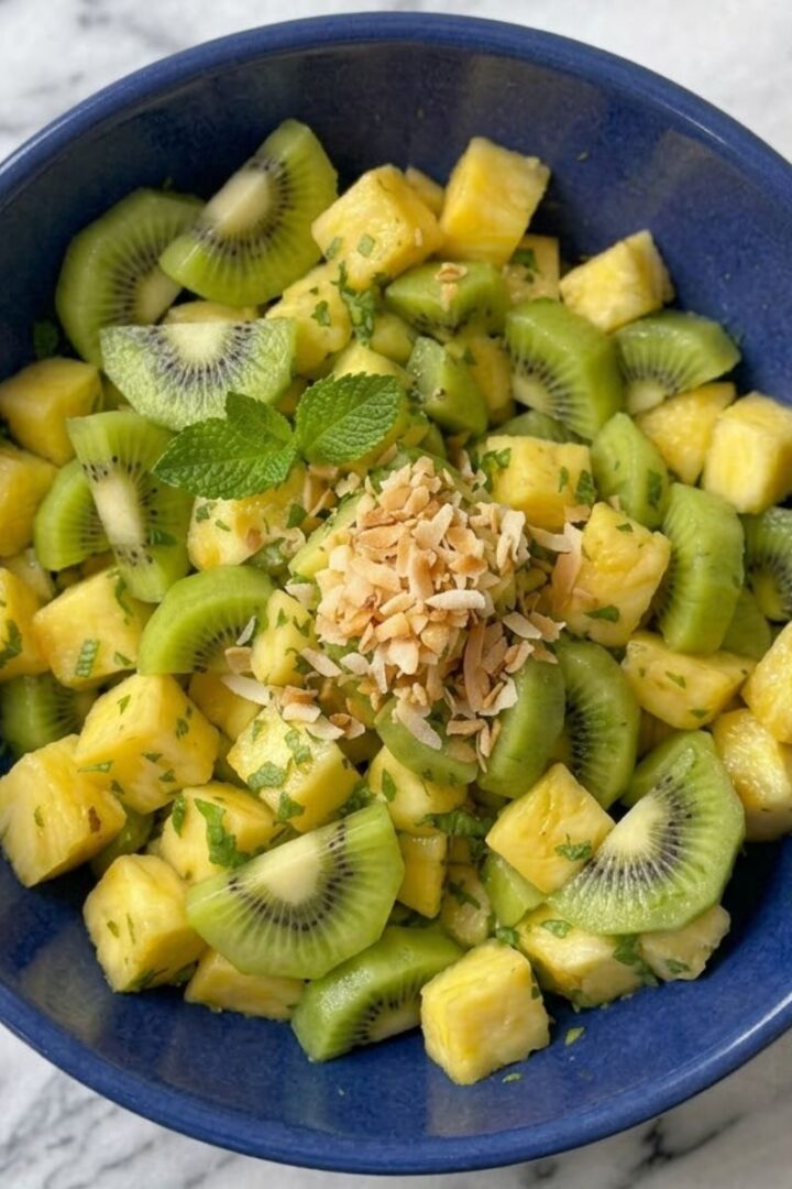 A close-up of Pineapple Kiwi Salad in a blue ceramic bowl placed on white marble kitchen counter.
