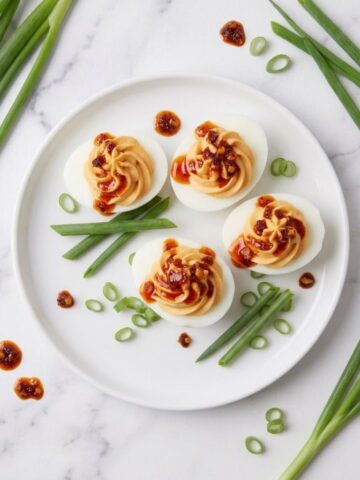 An overhead top-down angle of Spicy Chili Garlic Deviled Eggs place on a white simple plate with sliced chili and white onions all placed on a white marble kitchen counter.