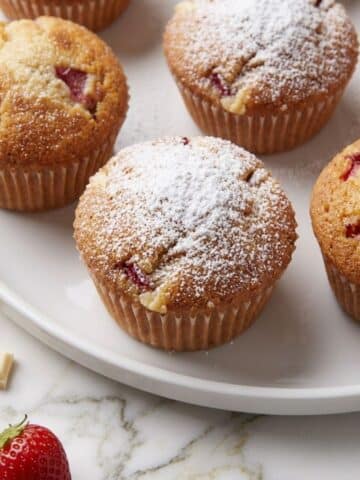 A close-up of baked White Chocolate Chip Strawberry Muffins on a white plate.