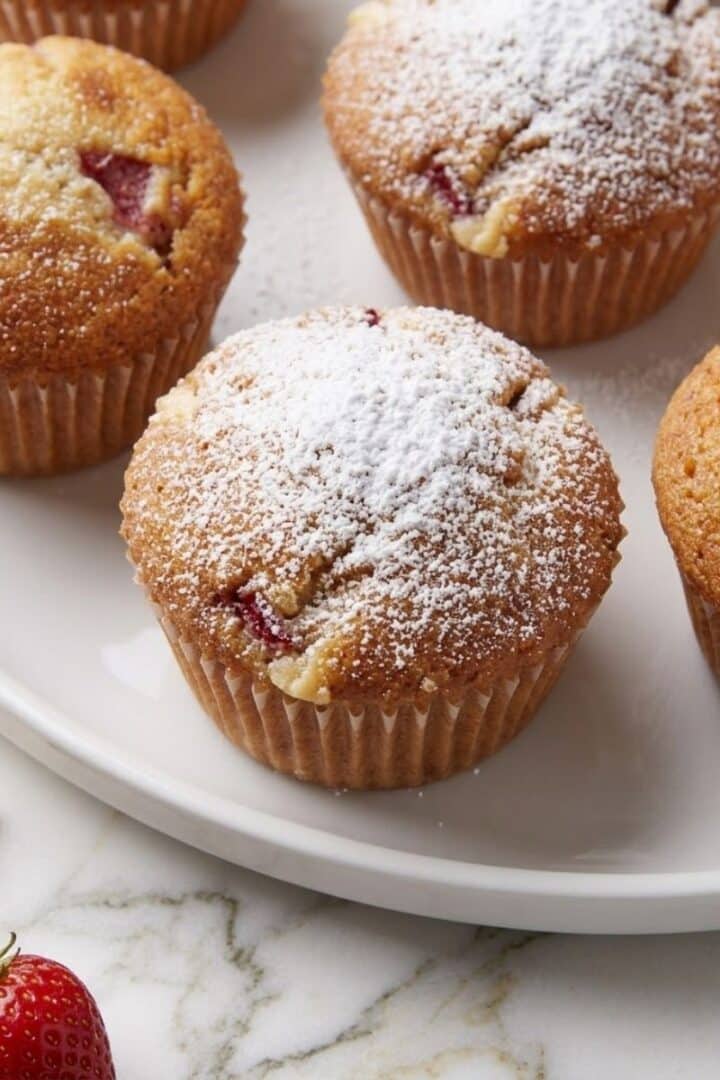 A close-up of baked White Chocolate Chip Strawberry Muffins on a white plate.