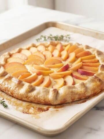 A close-up of the Apricot Honey Custard Galette golden and freshly baked with abricots place next to it. It's all placed on white marble kitchen counter with natural lighting.