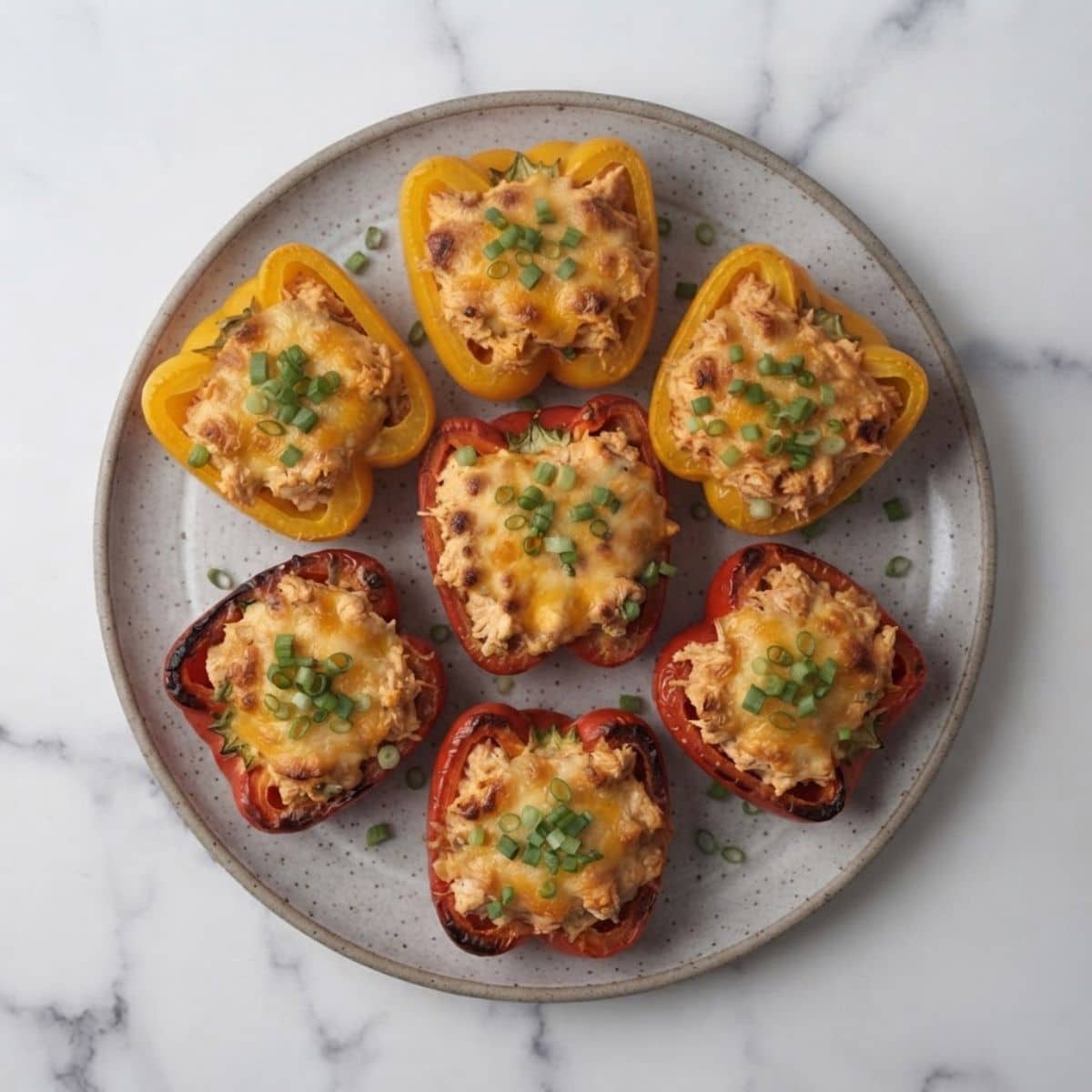 An overhead top-down view of Buffalo Chicken Stuffed Peppers placed on a grey ceramic plate with green onions sprinkled on top of them.