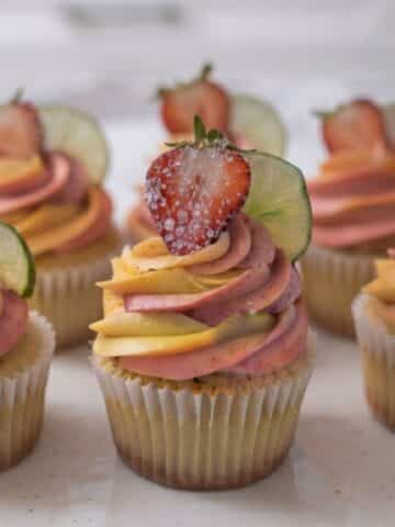 A close-up of Strawberry Mango Margarita Cupcakes placed on white marble kitchen counter with natural lighting.
