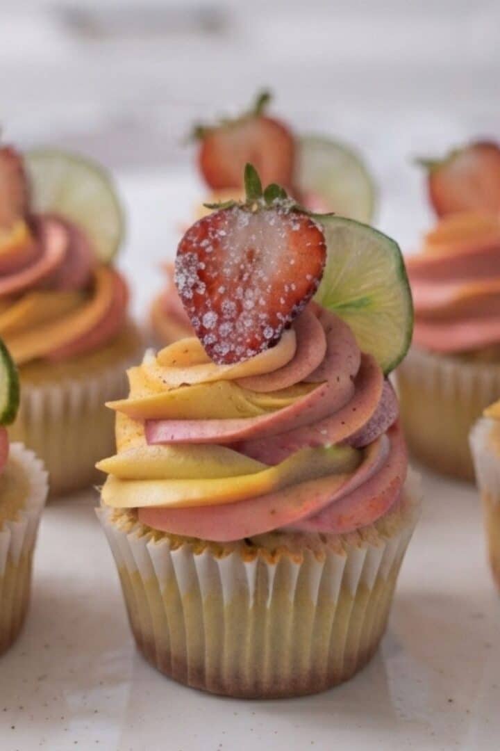 A close-up of Strawberry Mango Margarita Cupcakes placed on white marble kitchen counter with natural lighting.