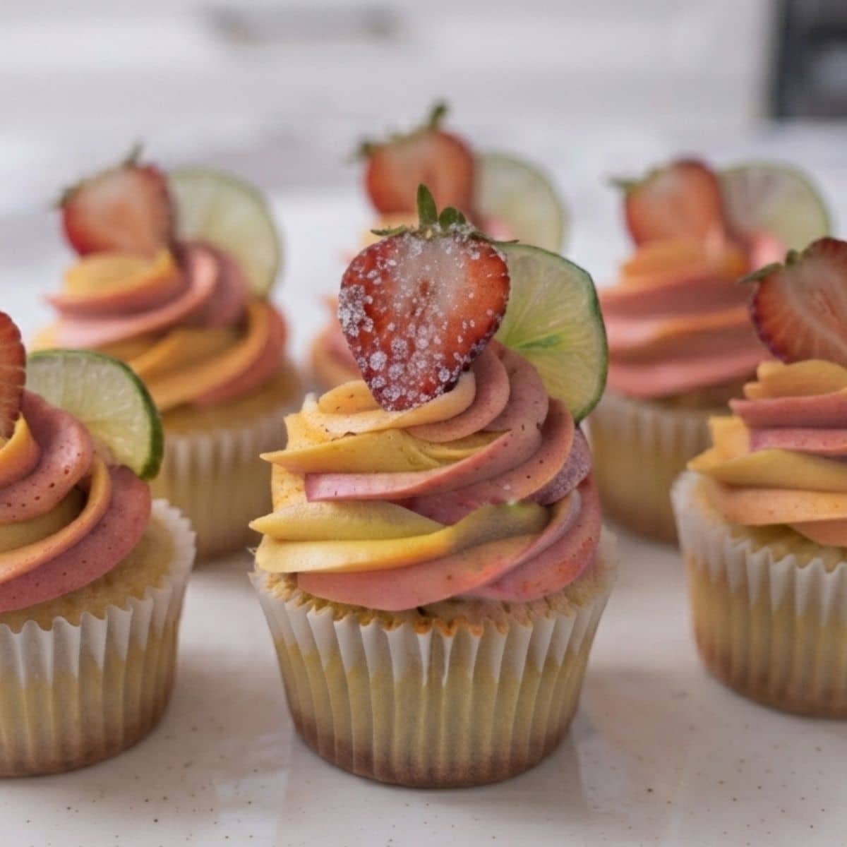 A close-up of Strawberry Mango Margarita Cupcakes placed on white marble kitchen counter with natural lighting.